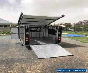 Enclosed motobike trailer with attached side tent and awnings.